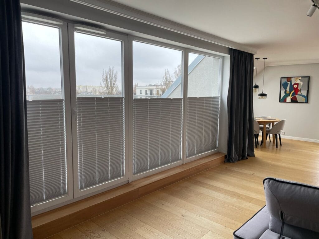 Plisy materiałowe w kolorze szarym – montaż w apartamencie w Łodzi Szare plisy materiałowe na wymiar zamontowane w drzwiach balkonowych – realizacja Veo Design Łódź